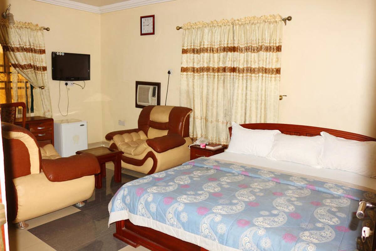 A hotel room with a bed, two armchairs, a desk, a television, and a window with curtains.