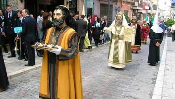 Escena callejera con una persona vestida con atuendo tradicional sosteniendo una bandeja, posiblemente para un evento cultural.