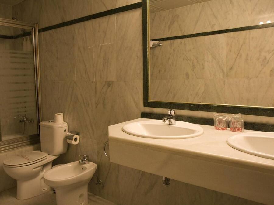 A bathroom with a toilet, bidet, and two sinks under a large mirror.