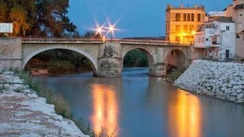 Un puente de piedra sobre un río tranquilo al anochecer, con luces de la calle reflejándose en el agua.