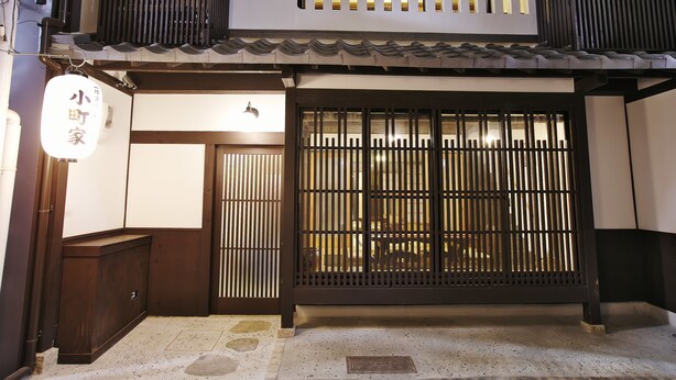 Un edificio japonés tradicional con fachada de madera, una puerta corredera de listones verticales y un letrero pequeño sobre la puerta.