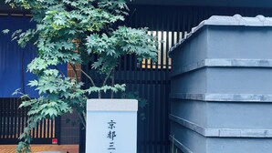 A stone planter with a tree, a stone sign with Chinese characters, and a modern building facade. - Kyoto Sanjo Ohashi (Kyoto)