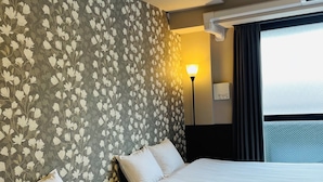 Quarto de hotel com duas camas, papel de parede floral, abajur e janela com cortinas.