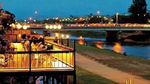 A riverside restaurant with outdoor seating, a bridge in the background, and city lights. - Kyoto Sanjo Ohashi (Kyoto)