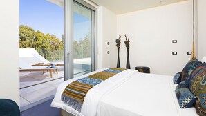 Une chambre moderne avec un grand lit, un balcon équipé de chaises longues et une vue sur les arbres.