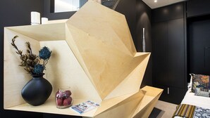 Un comptoir d’accueil moderne au design géométrique, un vase contenant des fleurs séchées et un verre de fruits.