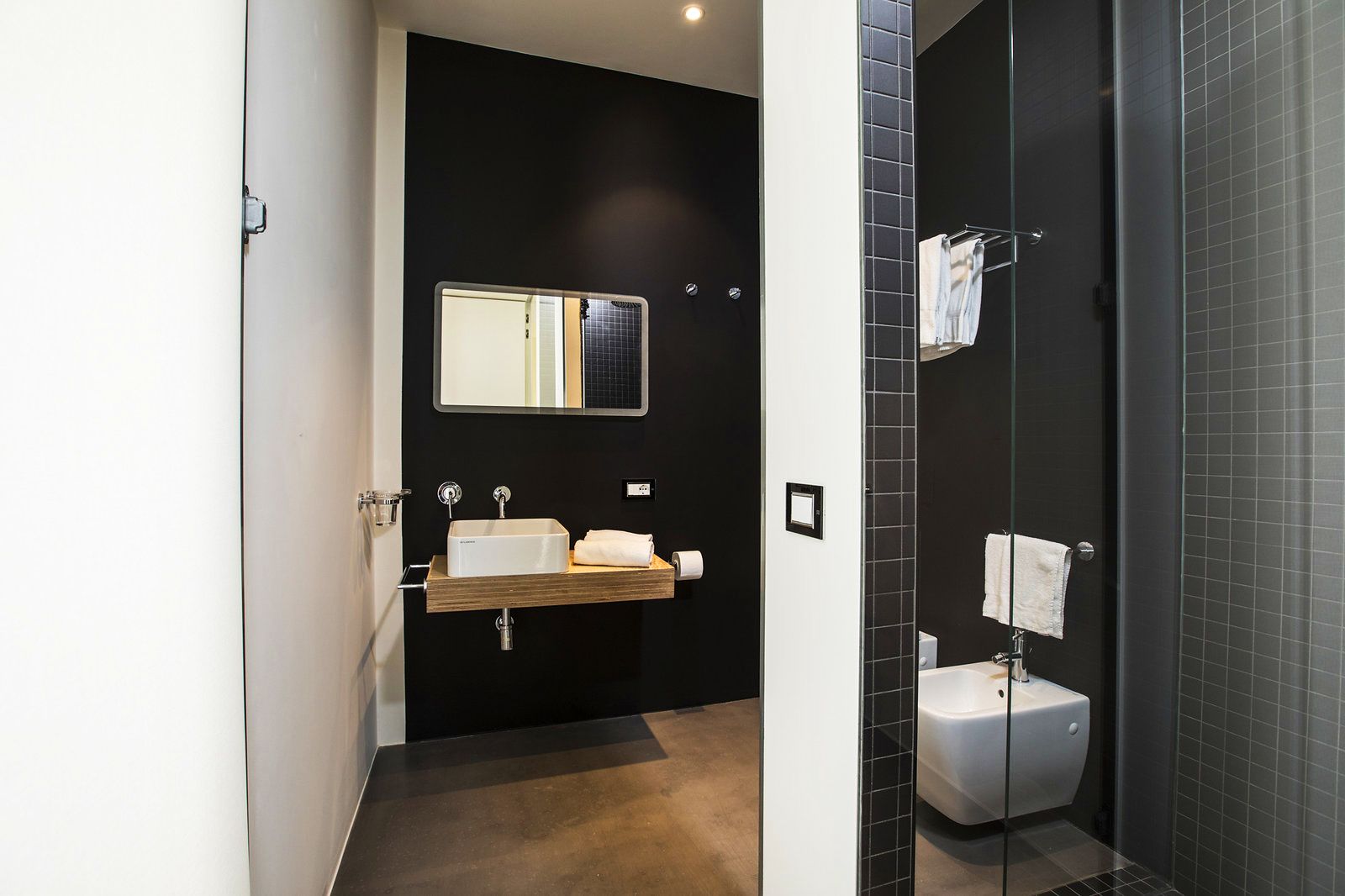 A modern bathroom with a dark wall, a mirror, a sink, and a toilet.
