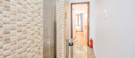 A hallway with a patterned wall, a fire extinguisher, and a door leading to a room.