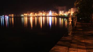 Vista noturna de um horizonte urbano à beira-mar, com edifícios iluminados refletindo na água.