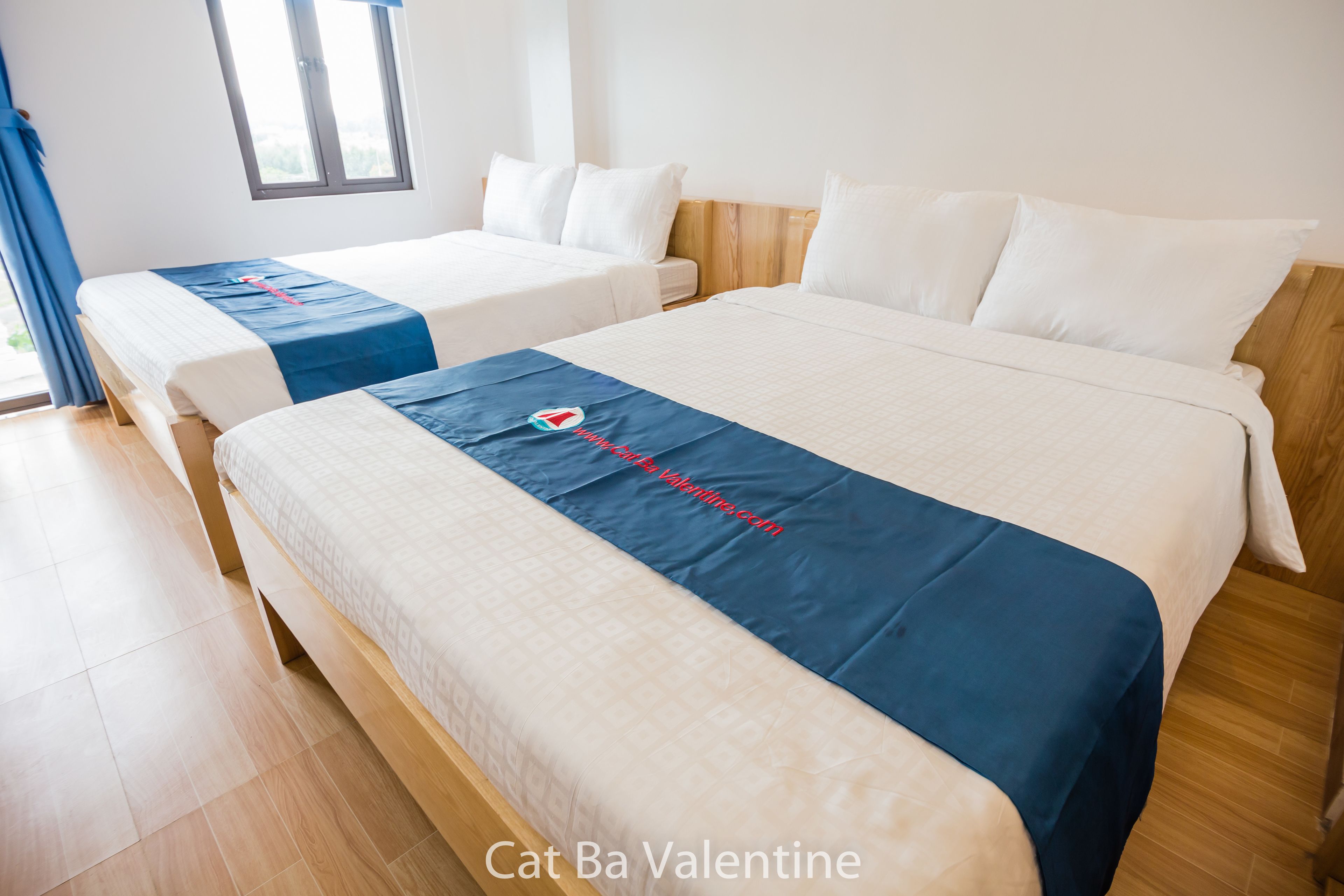 Quarto de hotel com duas camas, cabeceira de madeira e janela com cortinas.