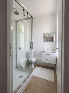 A modern bathroom with a glass shower enclosure, a toilet, a sink with a mirror, and a small rug on the floor. - Hôtel JurJura (Dole)