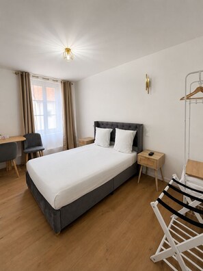 A hotel room with a bed, bedside tables, a desk, a chair, a hanging clothes rack, and a window with curtains. - Hôtel JurJura (Dole)