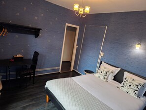 A bedroom with a bed, a desk, and a chair. There is a door leading to another room. - Hôtel JurJura (Dole)