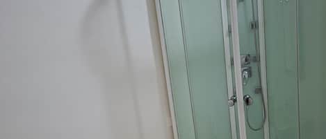 Ducha en esquina con mampara de vidrio, un perchero con dos toallas y un tapete blanco en el suelo.
