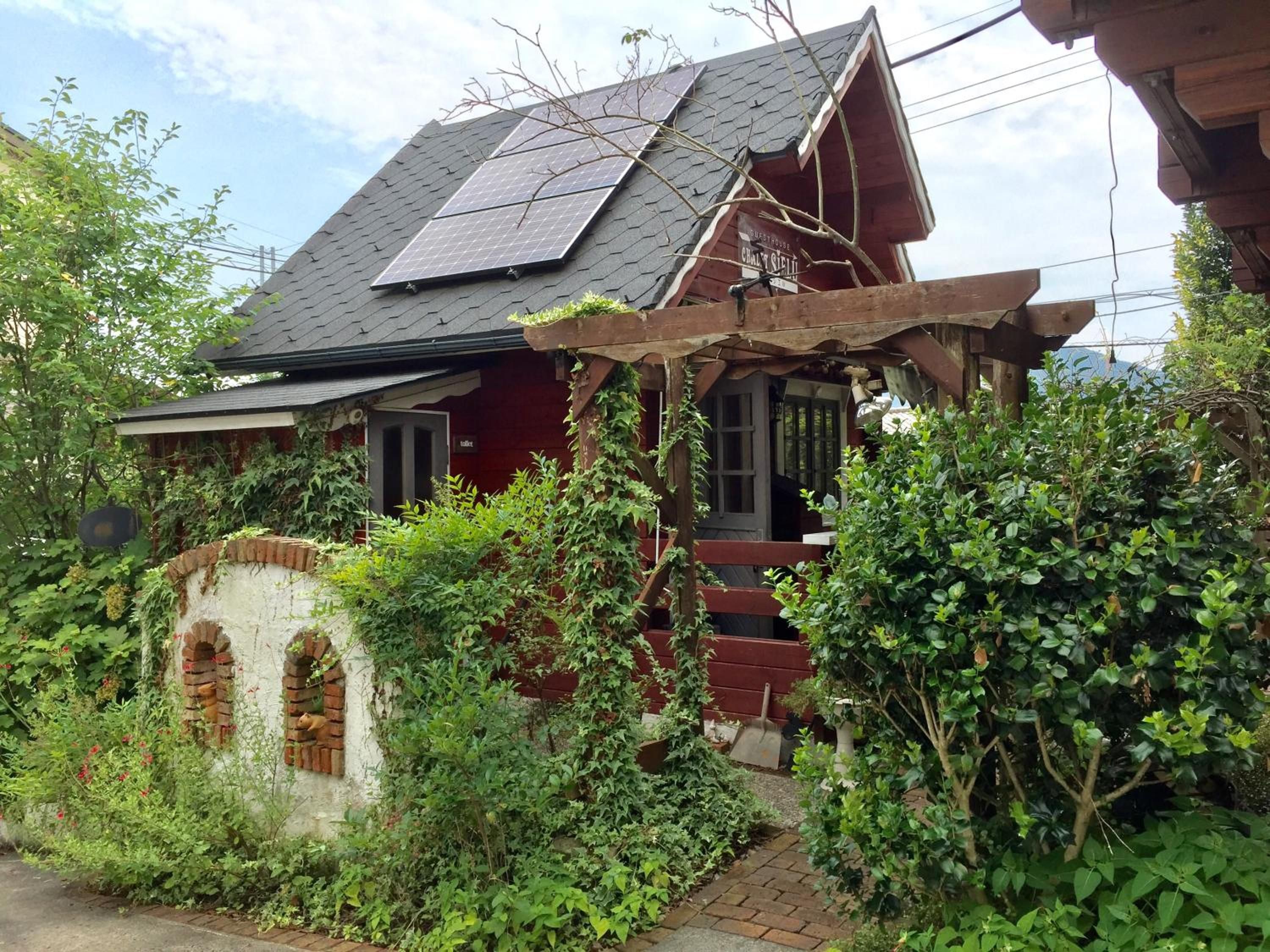 A rustic house with a sloped roof, solar panels, and a brick wall with arched windows.