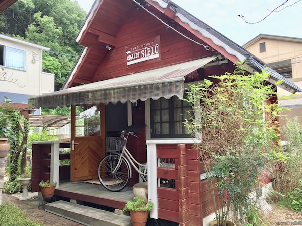 A guesthouse with a red exterior, a bicycle parked outside, and a sign indicating it is a guesthouse.