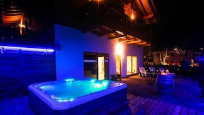 An outdoor hot tub area with a wooden deck, a seating area with chairs, and a wooden barrel. - Garni & Wellness Anderle (Vignola-Falesina)