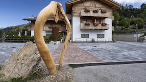 A wooden building with balconies and flower boxes, a large rock sculpture in the foreground, and a paved area in front. - Garni & Wellness Anderle (Vignola-Falesina)