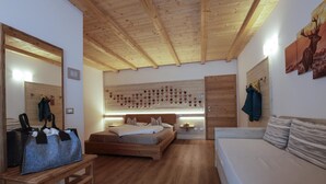 A bedroom with a wooden ceiling, a bed, a bench, a couch, and a wall with heart-shaped decorations. - Garni & Wellness Anderle (Vignola-Falesina)