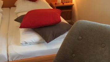 Habitación de hotel con cama, almohadas, mesita de noche con lámpara y una silla con toalla y pimientos rojos.
