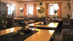 A dining area with wooden tables and chairs, pendant lights, and a cross on the wall.