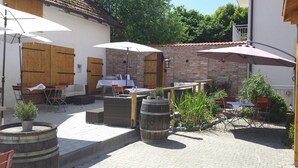 Un espace extérieur aménagé en terrasse, avec des tables et des chaises, des tonneaux en bois et des parasols pour créer de l’ombre.