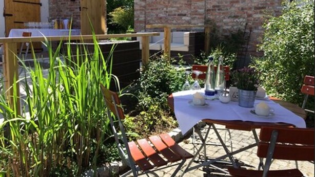 An outdoor dining area with a brick wall, wooden table, and chairs.