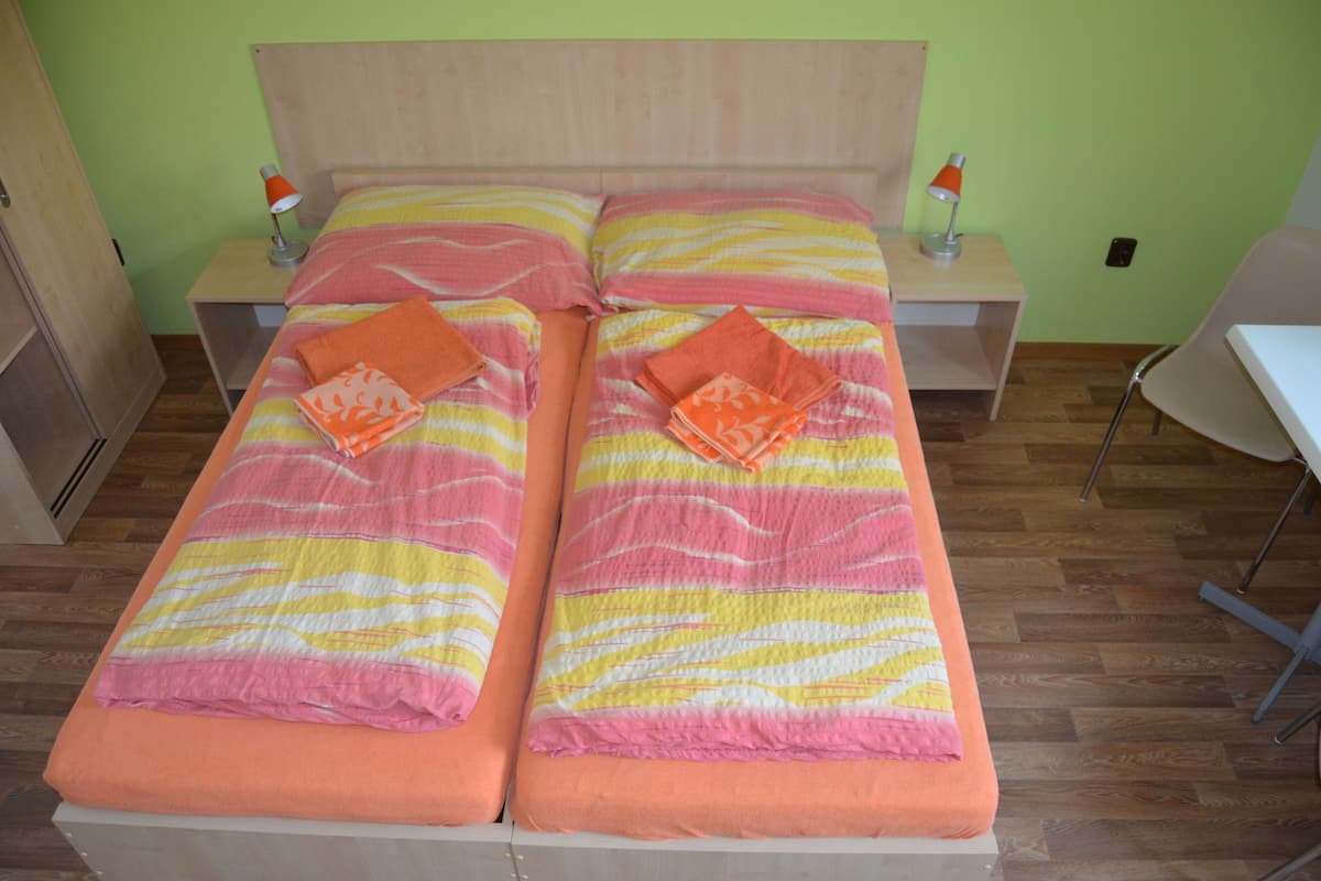 A twin bed with striped bedding, two bedside tables with lamps, and a chair in a room with wooden flooring and green walls.