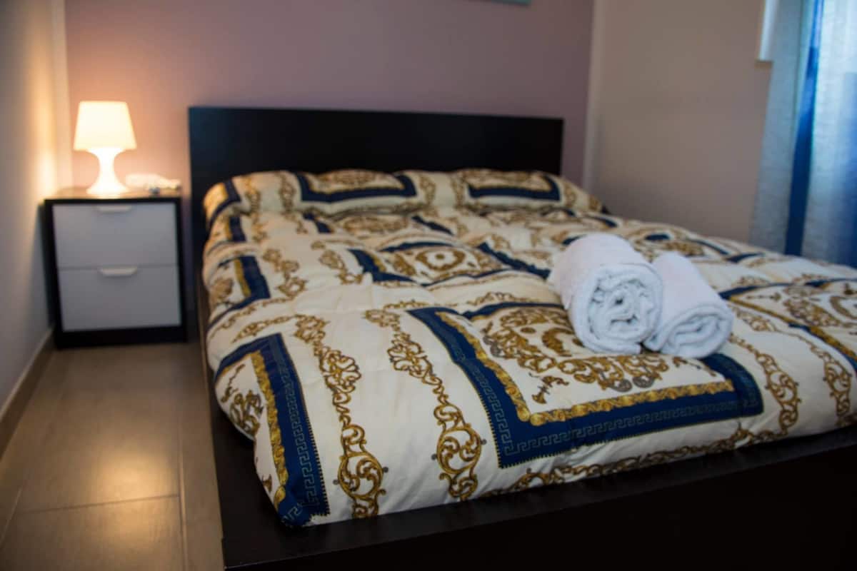A neatly made bed with a patterned bedspread, a folded towel, and a nightstand with a lamp.