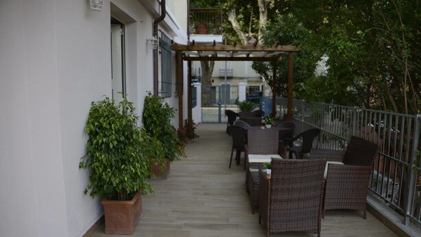 Eine Terrasse im Freien mit Korbmöbeln, Blumentöpfen und einer Pergola.
