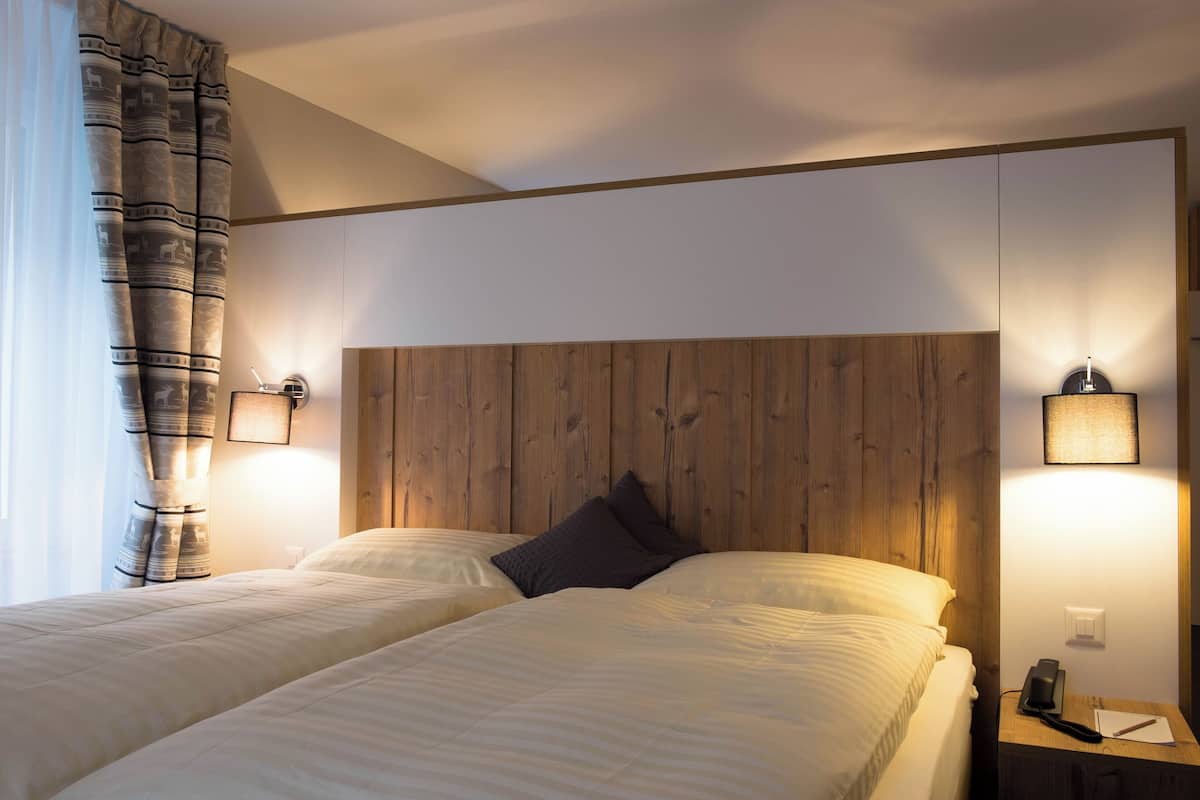 A hotel room with two beds, wooden headboard, bedside lamps, and a nightstand with a phone and notepad.