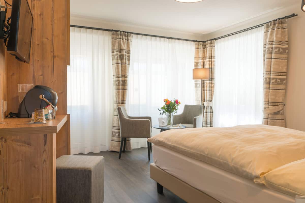 A hotel room with a bed, a desk, a chair, a lamp, and a window with curtains.