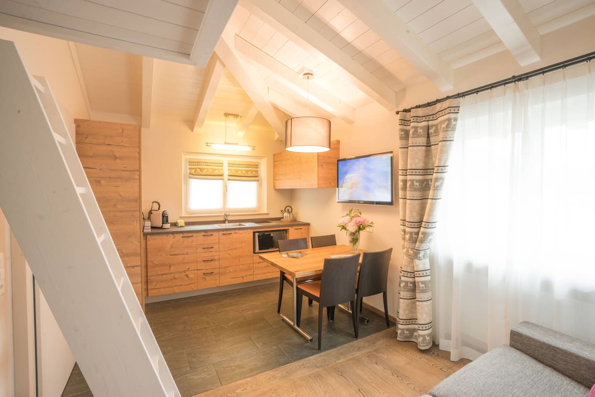 A modern kitchen with wooden cabinets, a dining table with chairs, and a TV mounted on the wall.