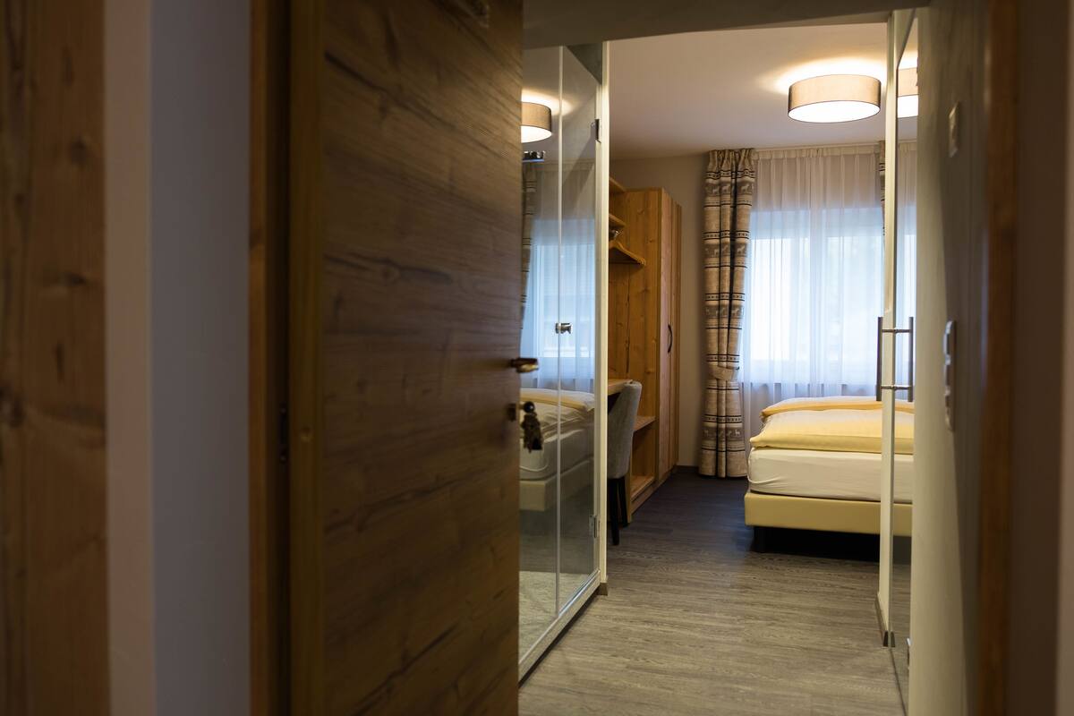 A hotel room with a wooden door, a bed, a desk, and a mirror.