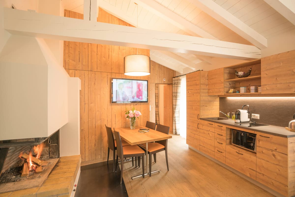 A modern kitchen with wooden cabinetry, a dining area with a table and chairs, a fireplace, and a television mounted on the wall.