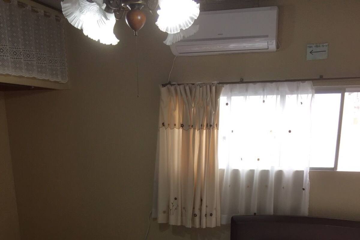 A bedroom with a bed, a window with curtains, an air conditioner, and a ceiling fan.