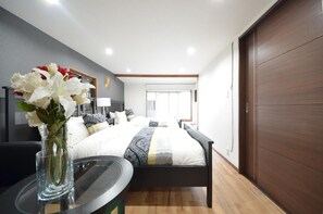 A modern hotel room with a large bed, bedside tables, a vase of flowers, and a view of the city. - Kyoto House (Kyoto)