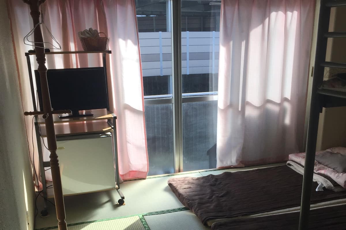 A room with tatami mats, a bunk bed, a TV on a stand, and a window with pink curtains.