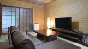 A traditional Japanese-style living room with tatami flooring, a low wooden table, a sofa, and a television. - Kyoto House (Kyoto)