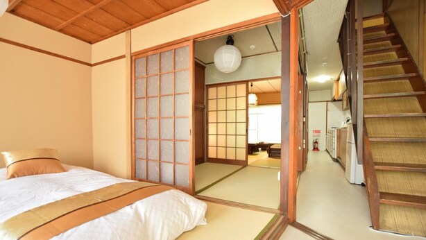 A traditional Japanese-style room with tatami flooring, a low wooden bed, sliding shoji doors, and a staircase leading to another level. - Kyoto House (Kyoto)