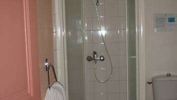 Une douche avec une porte en verre, une serviette blanche sur un porte-serviettes et des toilettes dans la pièce adjacente.