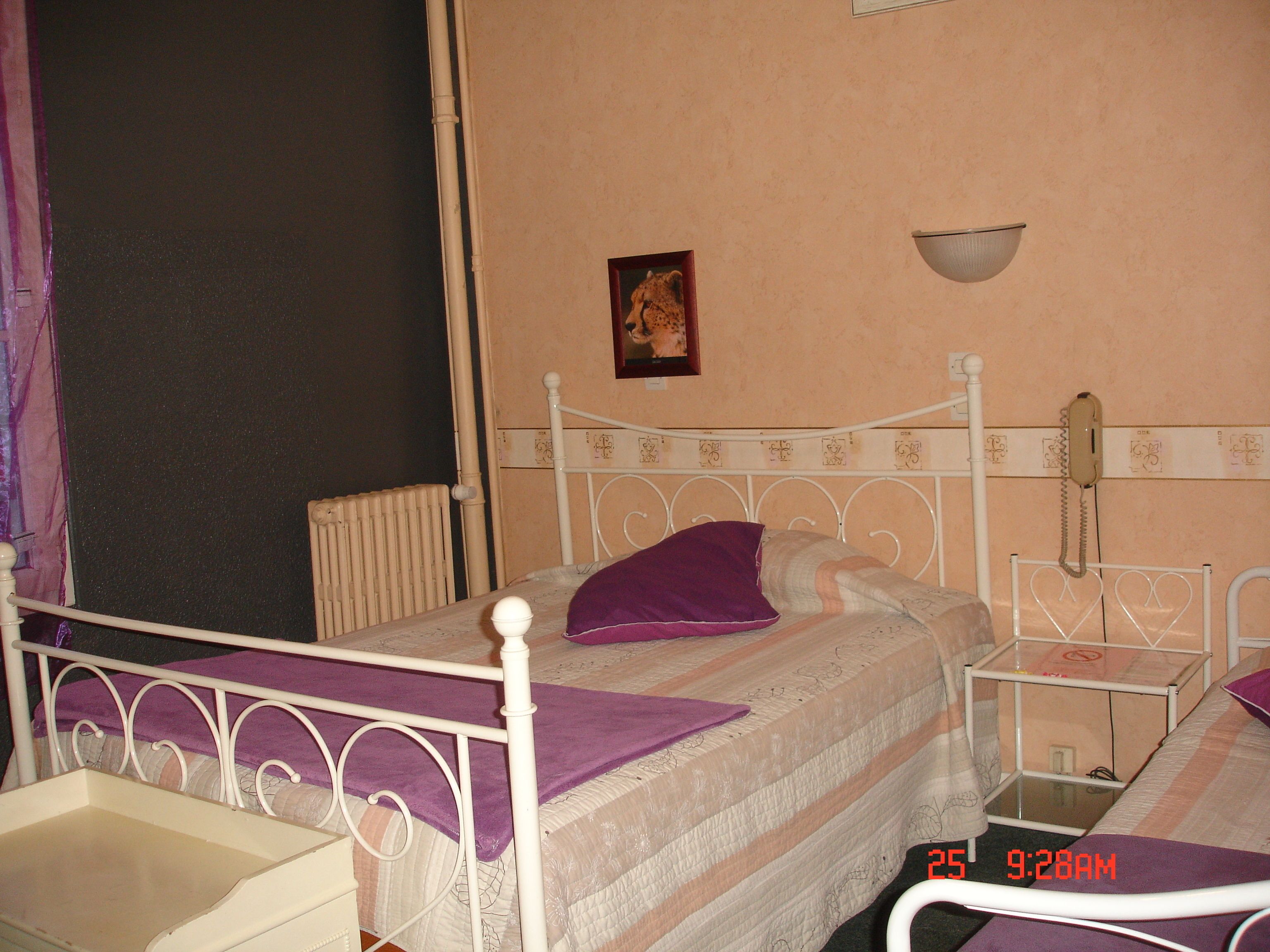 A single bed with a headboard, a bedside table, a nightstand, a wall-mounted telephone, and a picture frame on the wall.