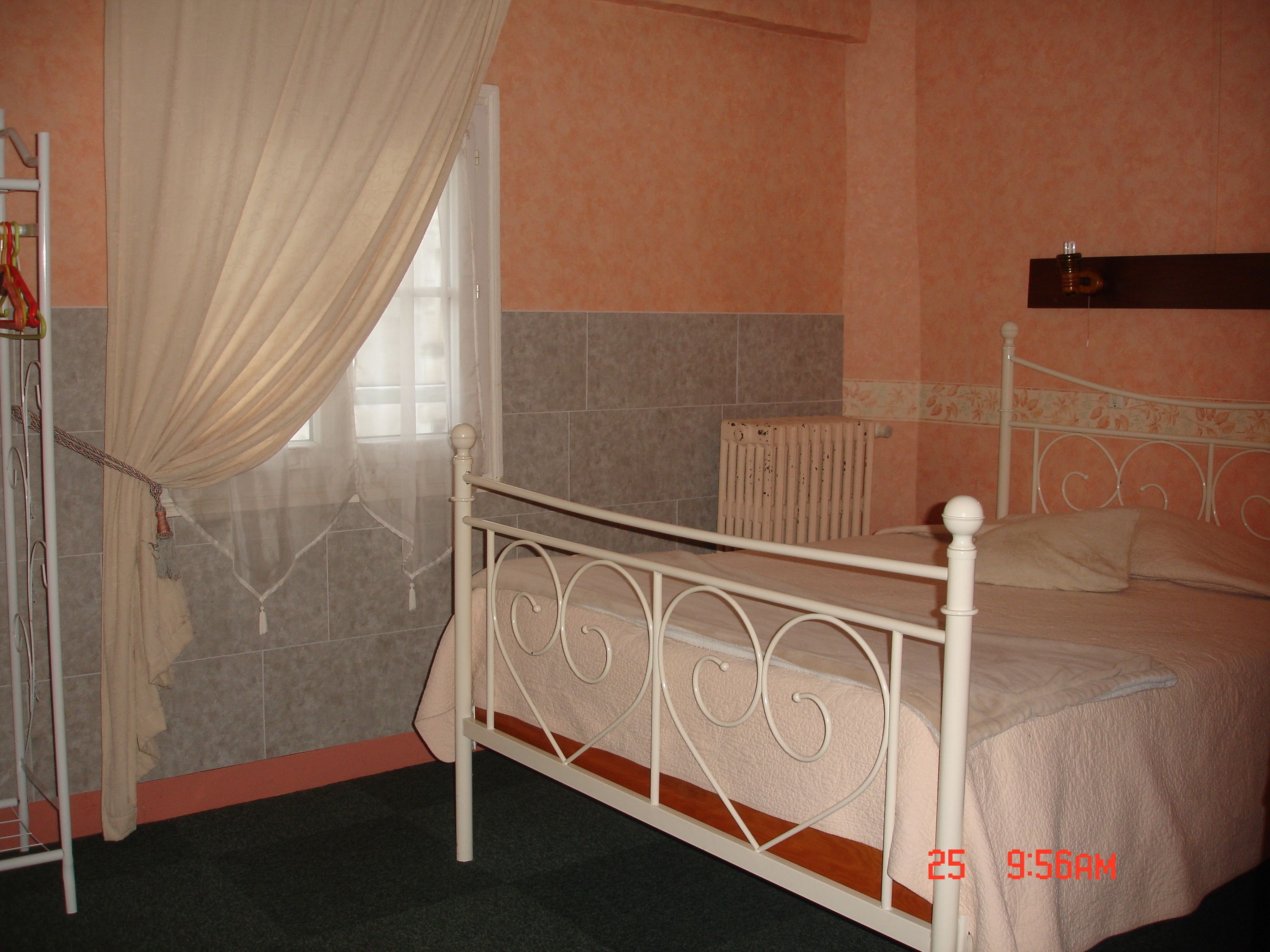 A bedroom with a bed, a radiator, and a window with curtains.