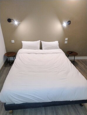 Una cama con ropa de cama blanca, dos mesitas de noche y lámparas fijadas a la pared.