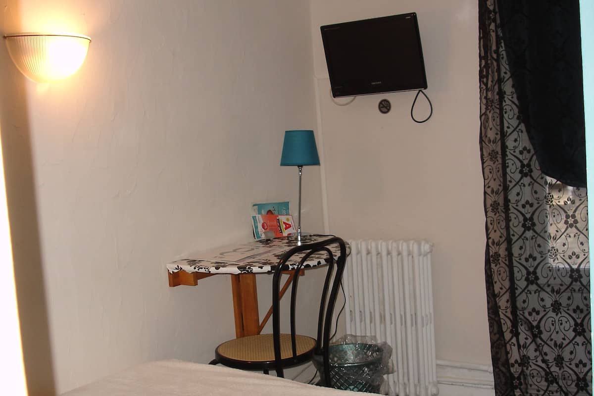 Ein Schlafzimmer mit Bett, Schreibtisch, Stuhl, Lampe, Heizkörper und Fernseher.