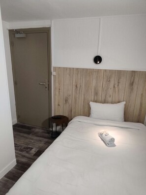 Una habitación de hotel con cabecera de madera, una cama con ropa blanca, una mesita de noche y una puerta.