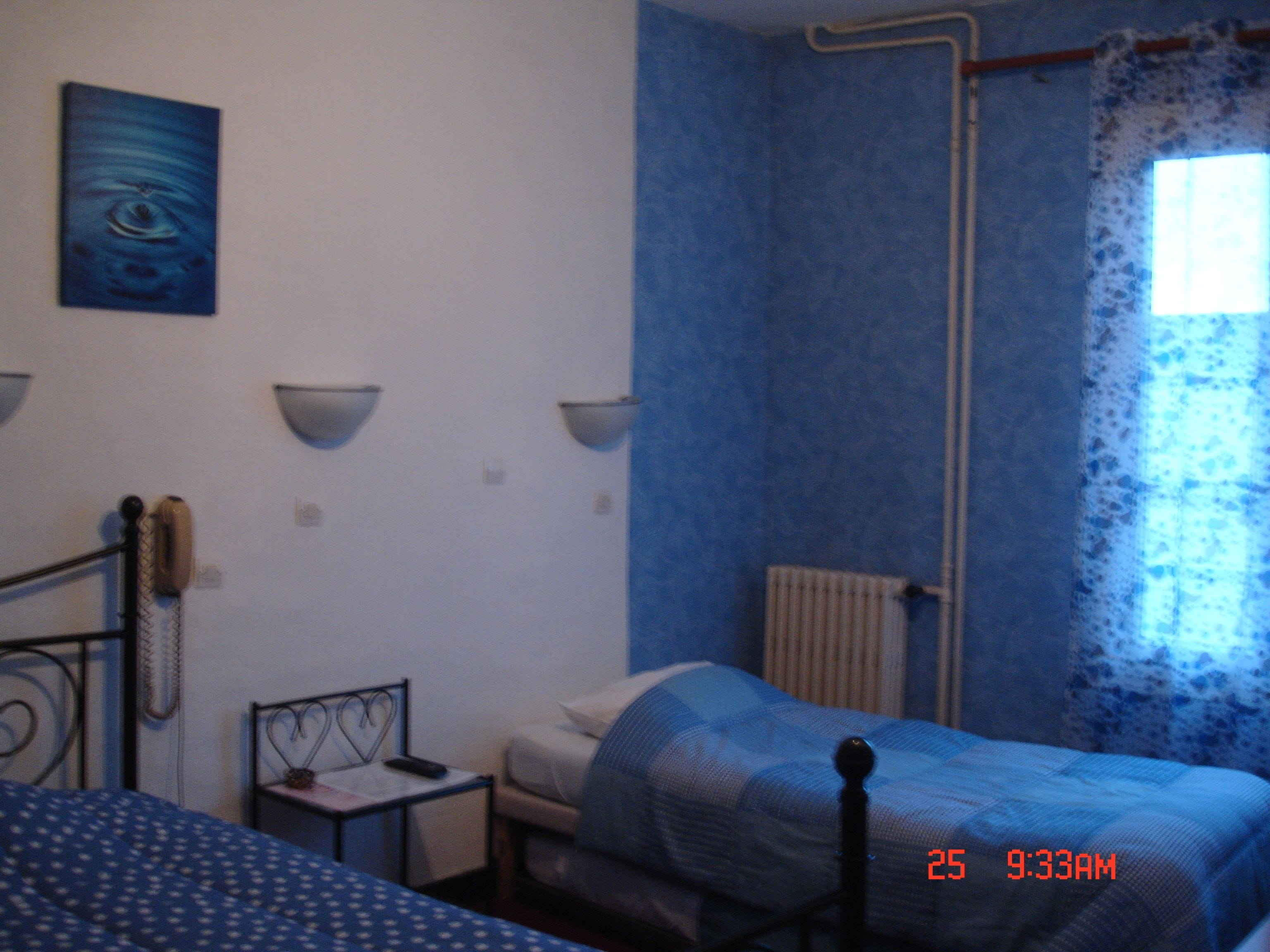 A bedroom with a bed, a chair, a small table, and a wall-mounted telephone.