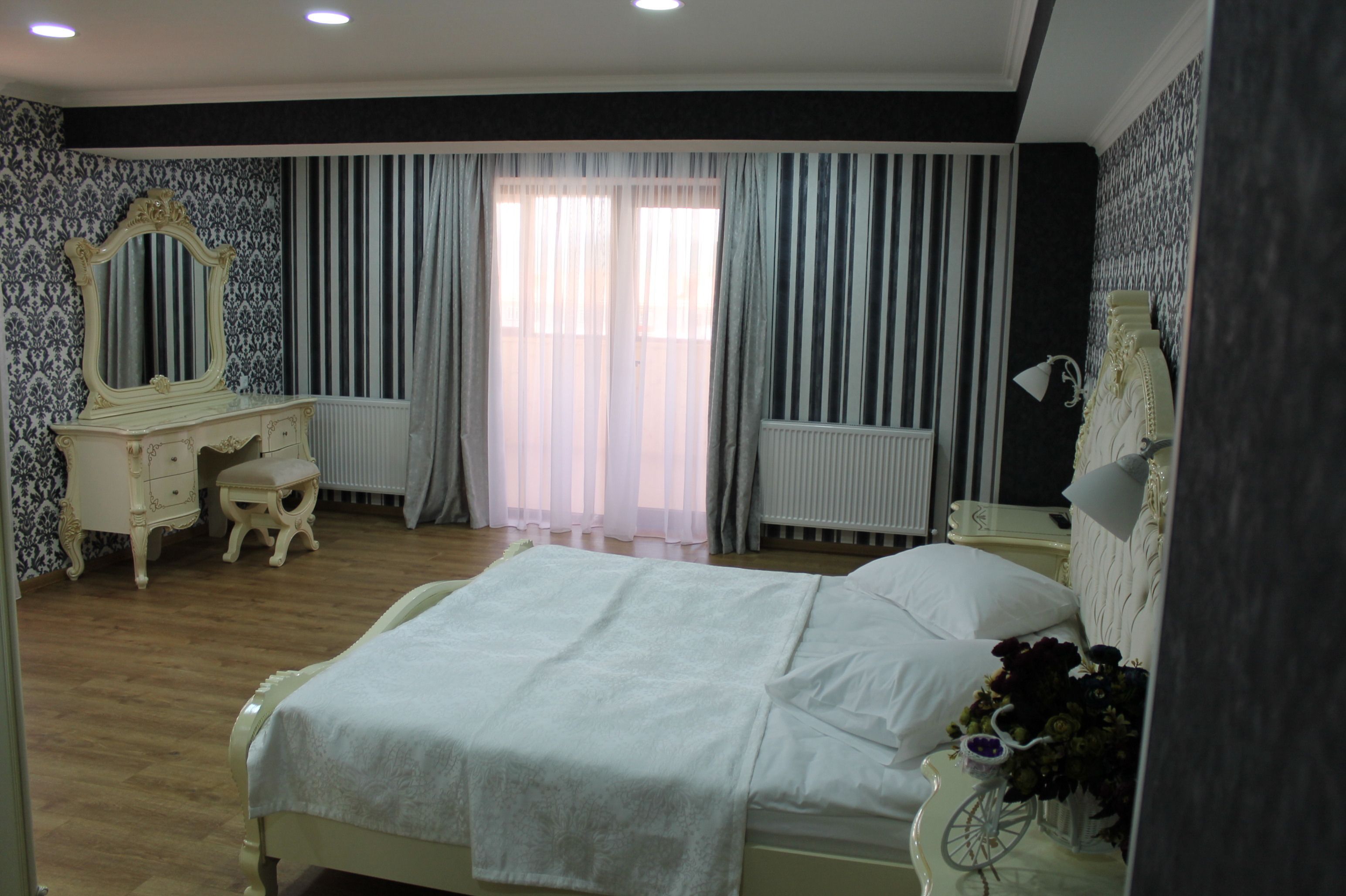 Un dormitorio con cama, tocador con espejo, radiador y ventana con cortinas.