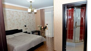 A bedroom with a bed, a nightstand, a vase with flowers, and a shower area with a red curtain. - Grand Palace (Akhaltsikhe)