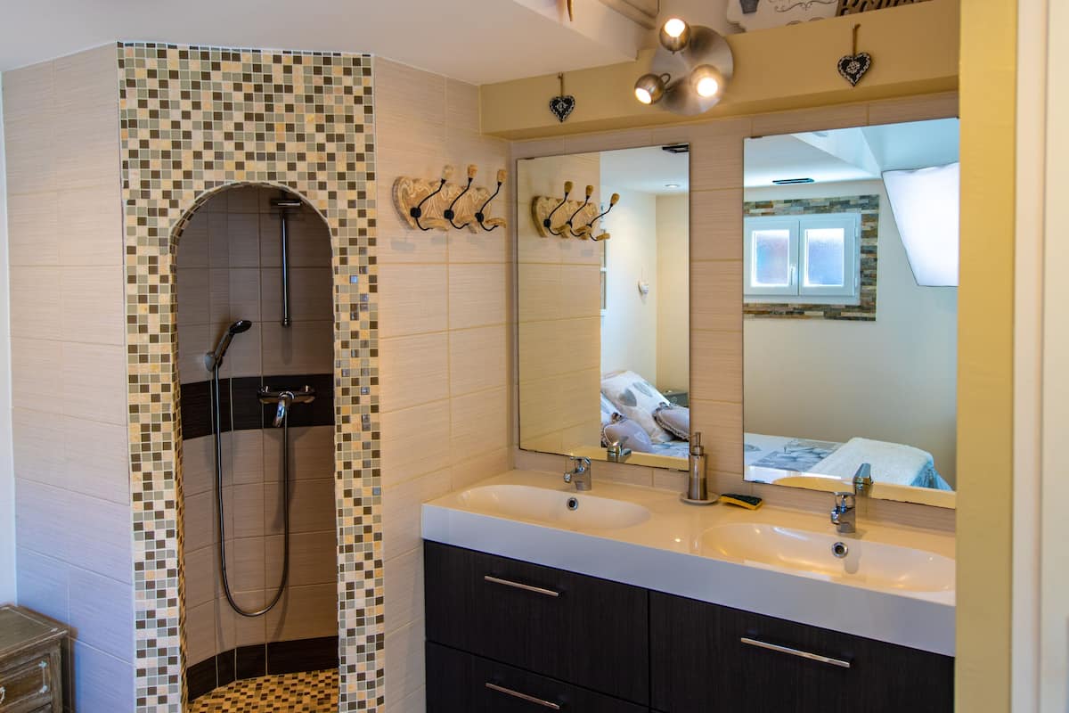 A bathroom with a shower, two sinks, a large mirror, and a towel rack.
